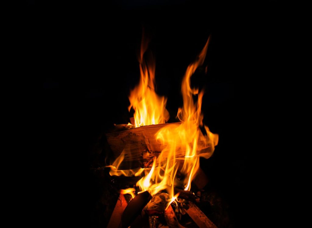 Bright campfire flames dance against a dark night backdrop, creating warmth and light.